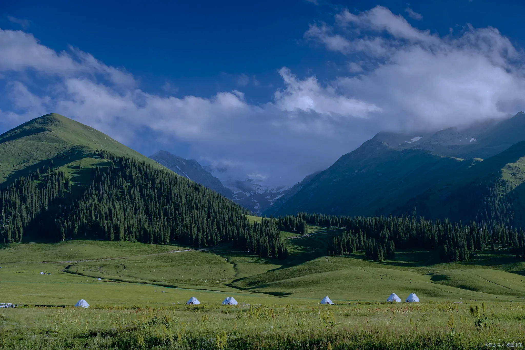 White Kazakh yurts sit on a wide green valley under cloud and snow-capped Tianshan peaks on the way to Zhaosu